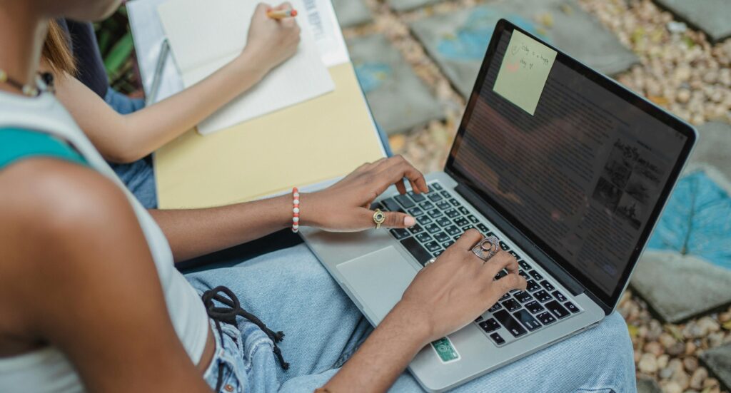 Crop faceless diverse students using laptop in park