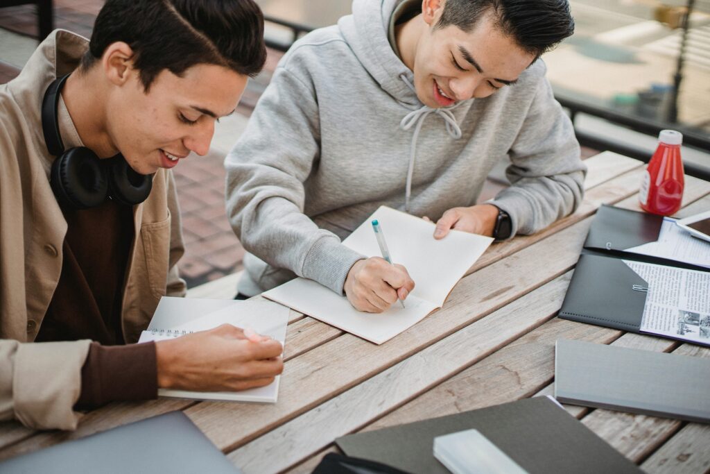 Crop positive diverse male students working on assignment in park